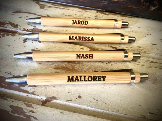 Four wooden pens with engraved names on a rustic wooden surface