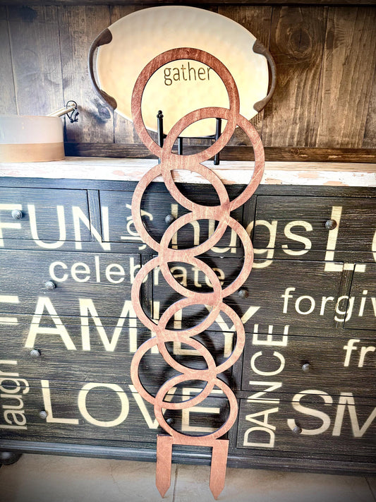 Colossal Small Circle Pattern plant trellis in a reddish-brown finish standing in front of a rustic wooden word sign wall