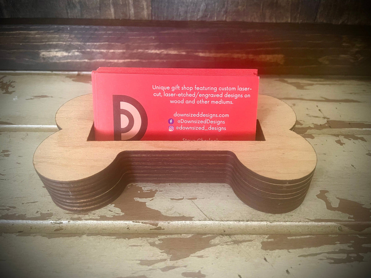 A dog bone shaped wood business card holder in a warm stain finish, holding business cards on a desk.