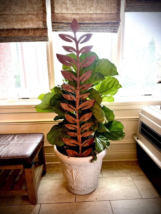 Colossal Leafy Vine plant trellis in a gunstock finish supporting a leafy green houseplant in a white decorative planter in front of a window
