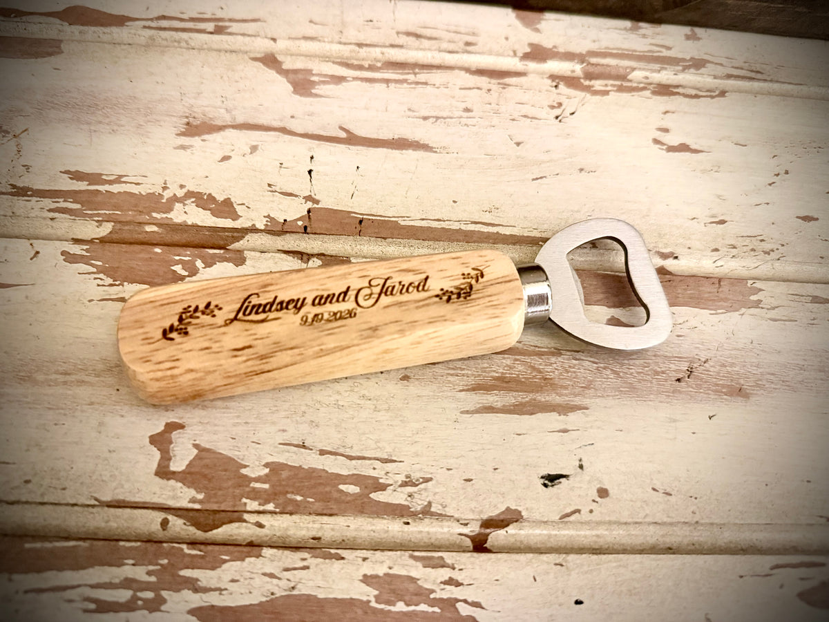 Personalized wooden wedding favor bottle opener engraved with the couple’s names and wedding date, displayed on a distressed white wood surface
