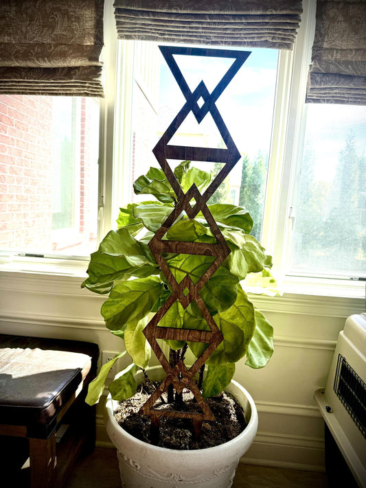 Walnut Colossal Inverted Triangle indoor plant trellis supporting a large leafy houseplant in a white pot beside a bright window