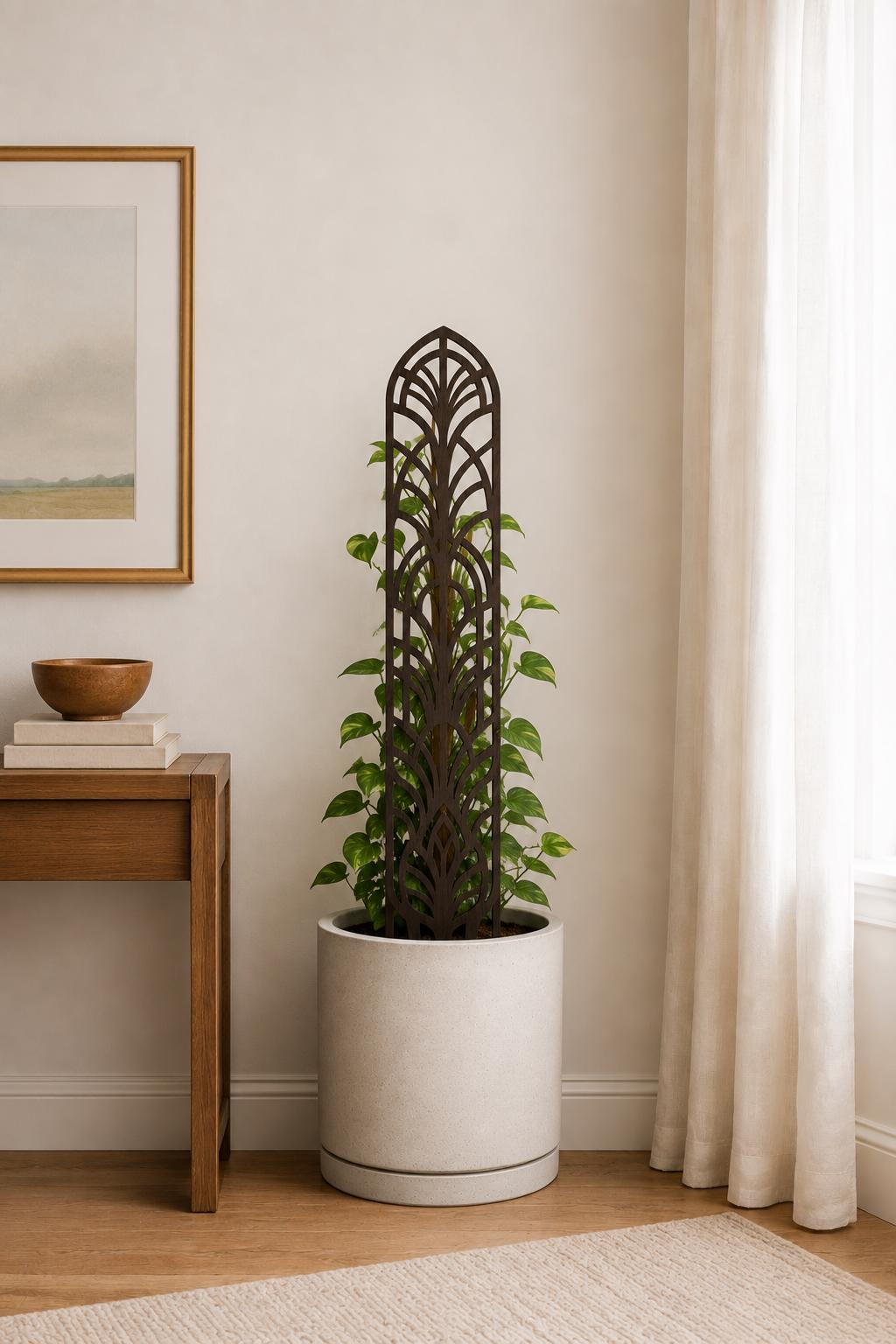 Colloquial arch plant trellis supporting a leafy climbing houseplant in a white planter beside a wood console table and tall curtained window in a modern living room.