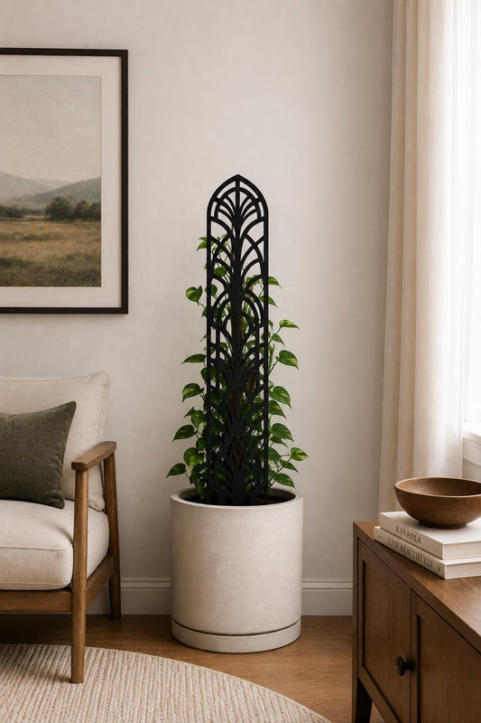 Colloquial arch plant trellis supporting a leafy climbing houseplant in a tall white planter beside a cream armchair and bright window in a modern living room.