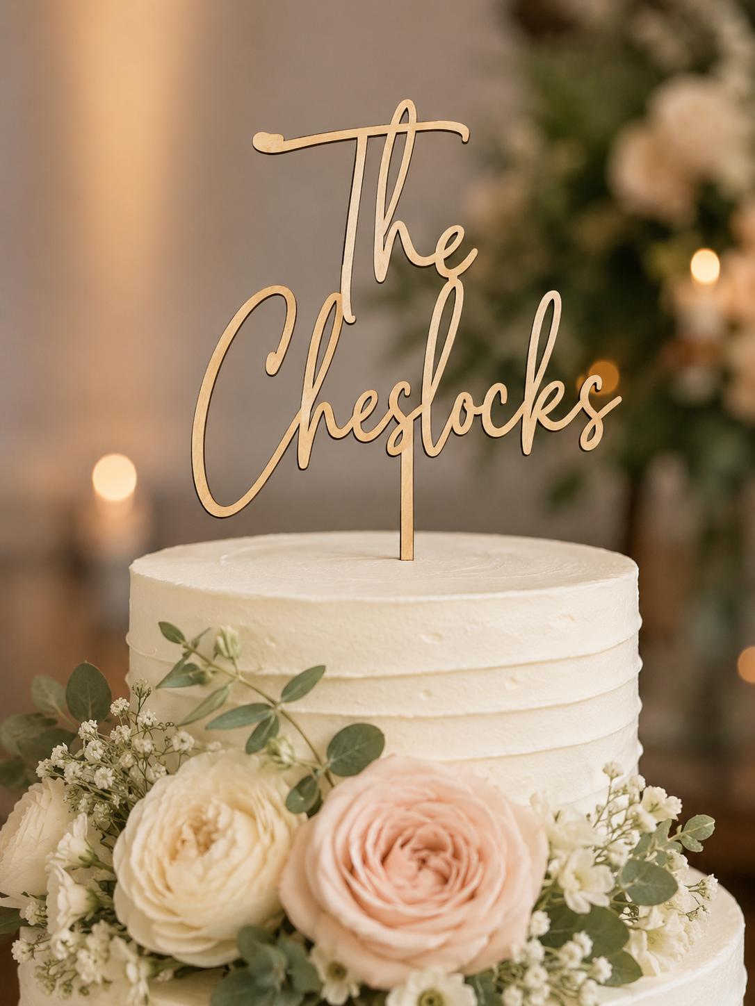 Personalized light wood script cake topper styled with greenery and white flowers