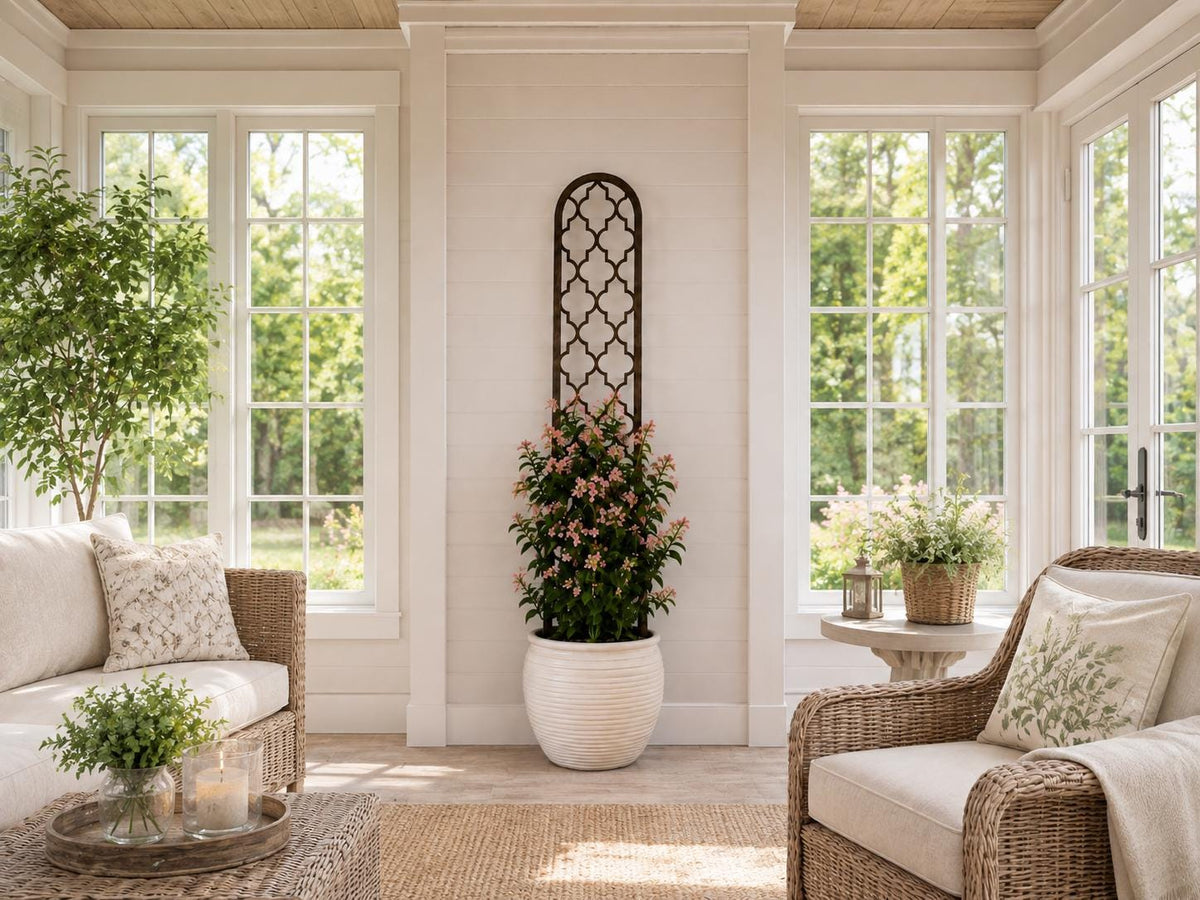 Colossal Quatrefoil plant trellis in dark walnut finish supporting a flowering climbing plant in a white ribbed pot, styled in a bright sunroom with wicker furniture