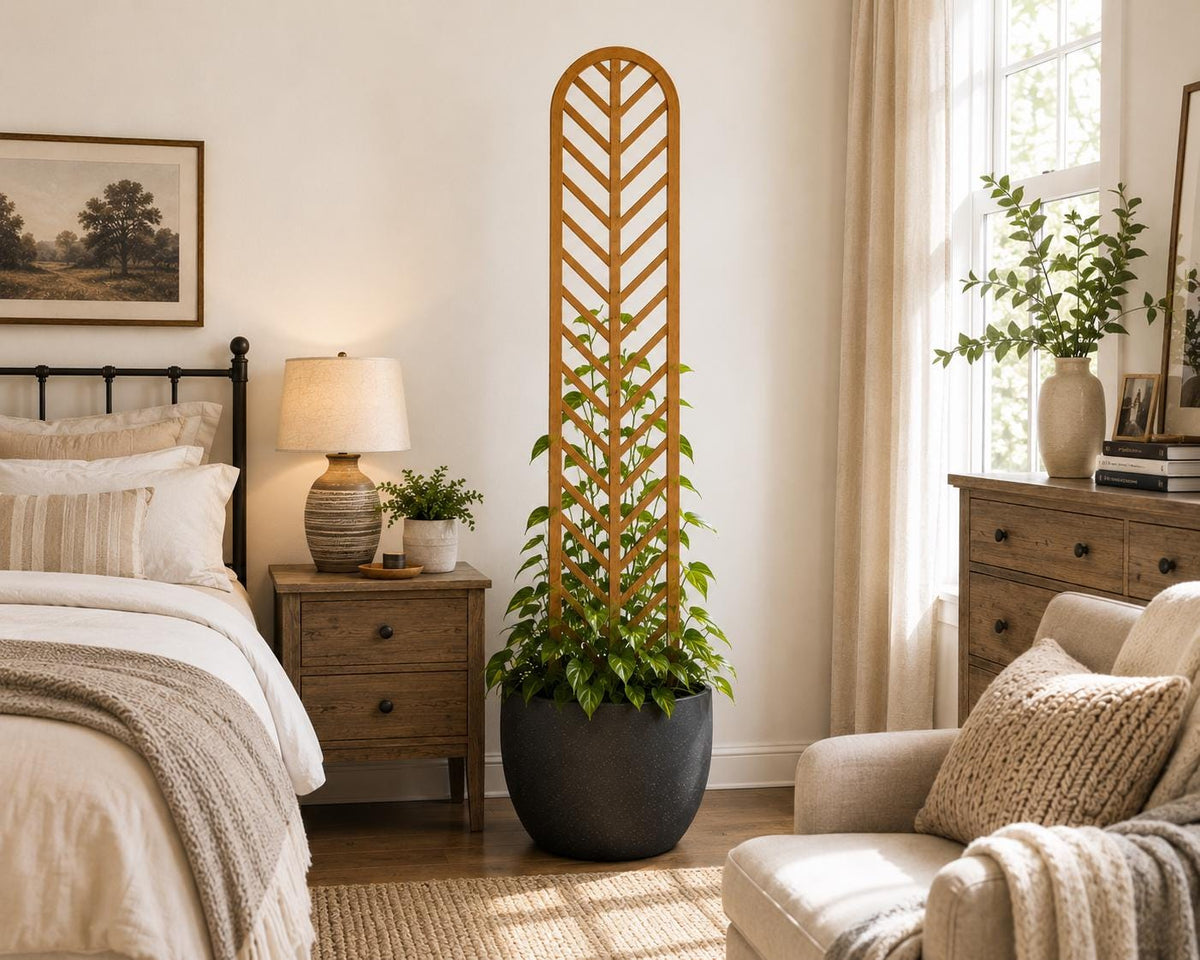 Colossal Herringbone indoor plant trellis in golden oak finish supporting a climbing plant in a black round pot, styled in a warm farmhouse bedroom with linen bedding and wood nightstand