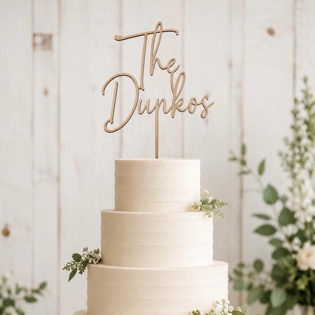 Black and white photo of a personalized script wood cake topper on a wedding cake