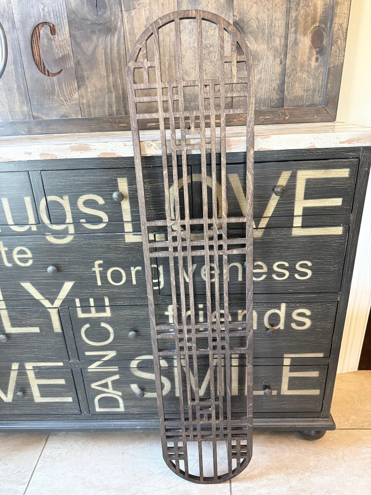 Colossal Art Deco hanging rack in a dark stain standing upright against a rustic wood cabinet