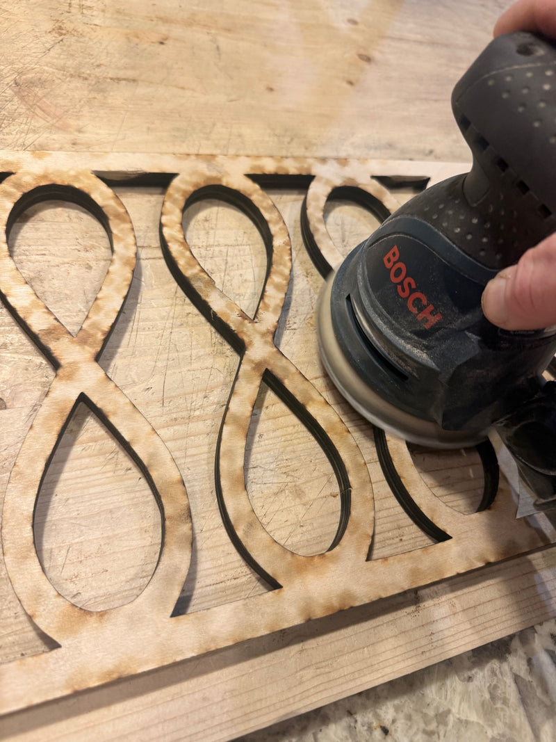 A hand sanding a freshly laser-cut wood panel in the Downsized Designs workshop