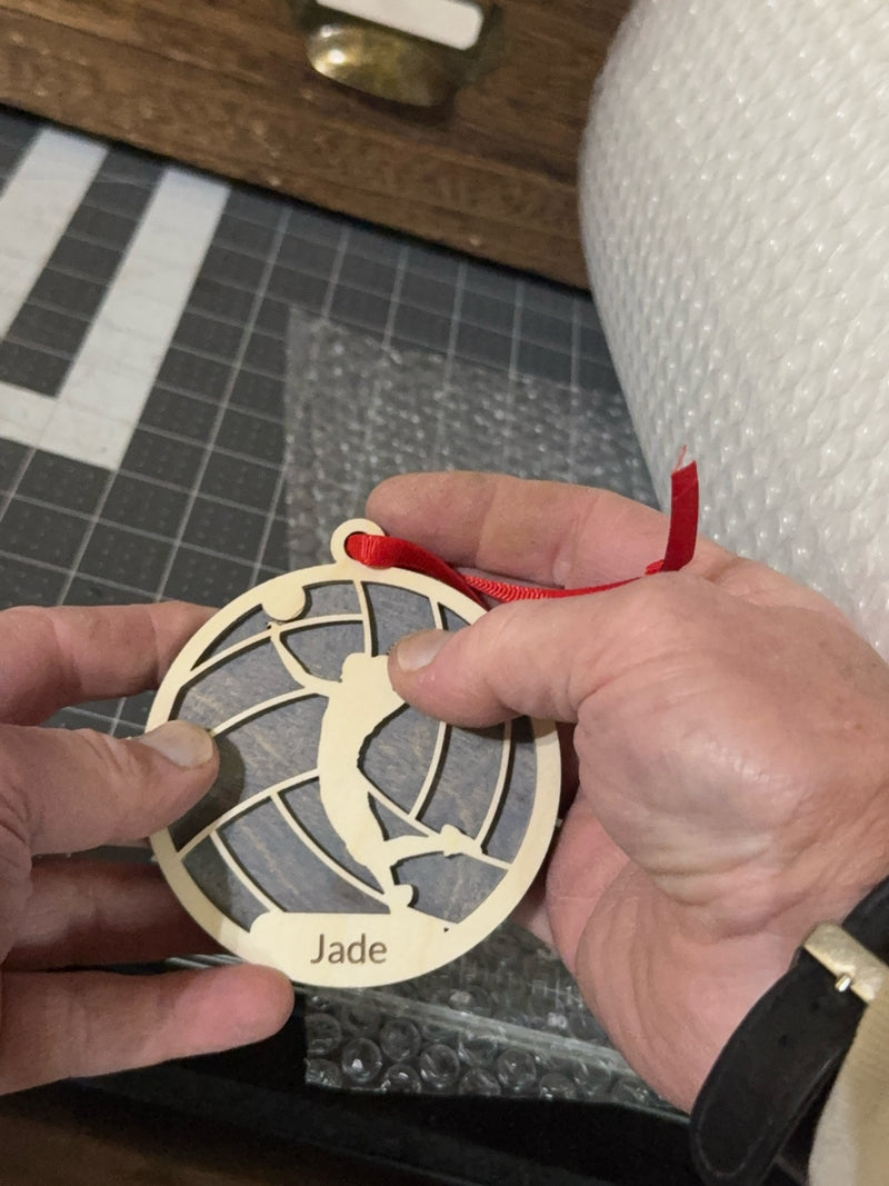 Hands checking a finished personalized wood volleyball ornament engraved with the name Jade